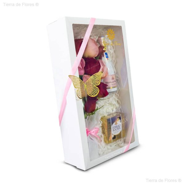 Arreglo floral en caja blanca con lazo rosado rosas en el interior caja de chocolates Noggy y un espumante vista lateral